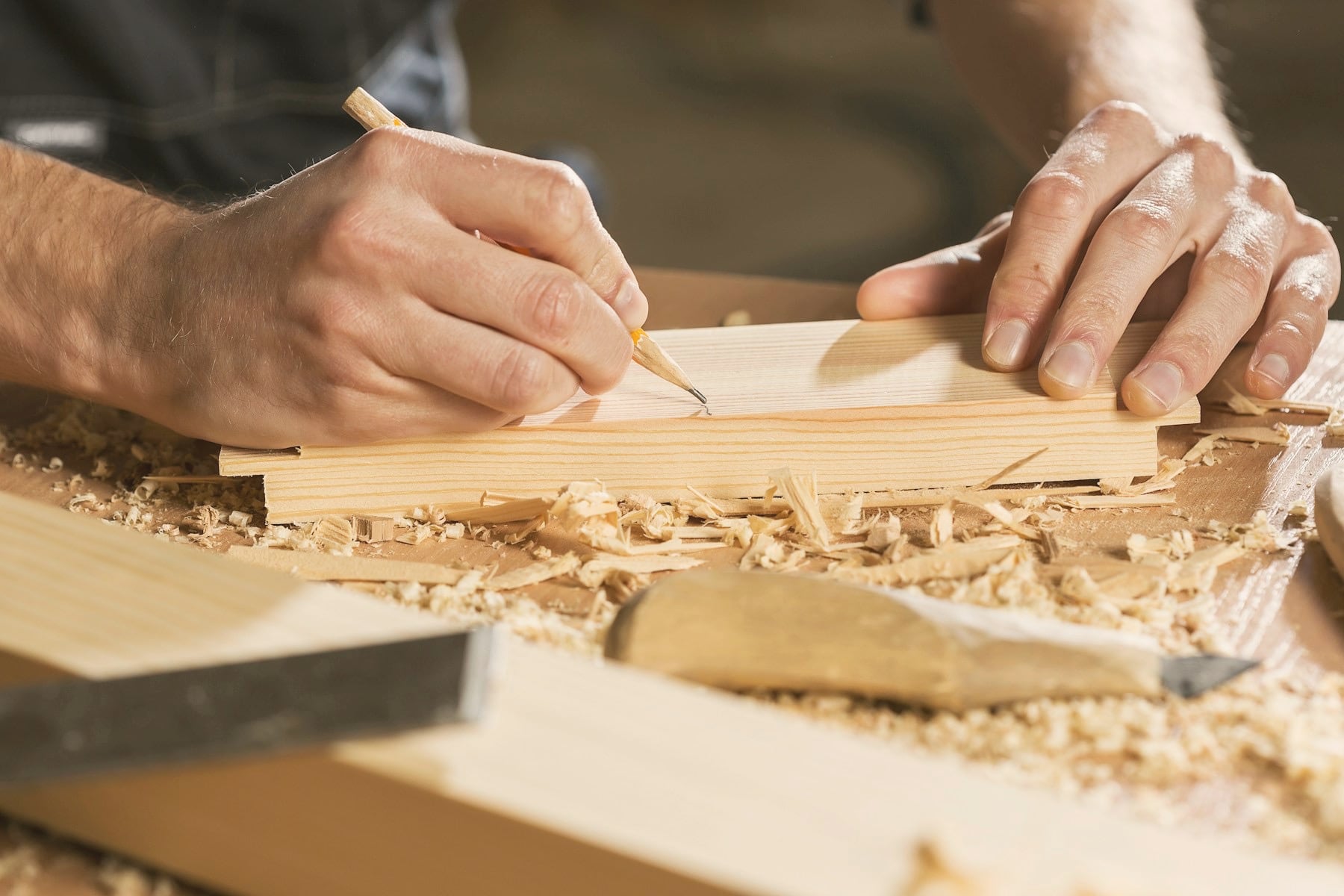 Mains d&rsquo;ébéniste traçant au crayon sur une pièce de bois, copeaux sur l&rsquo;établi