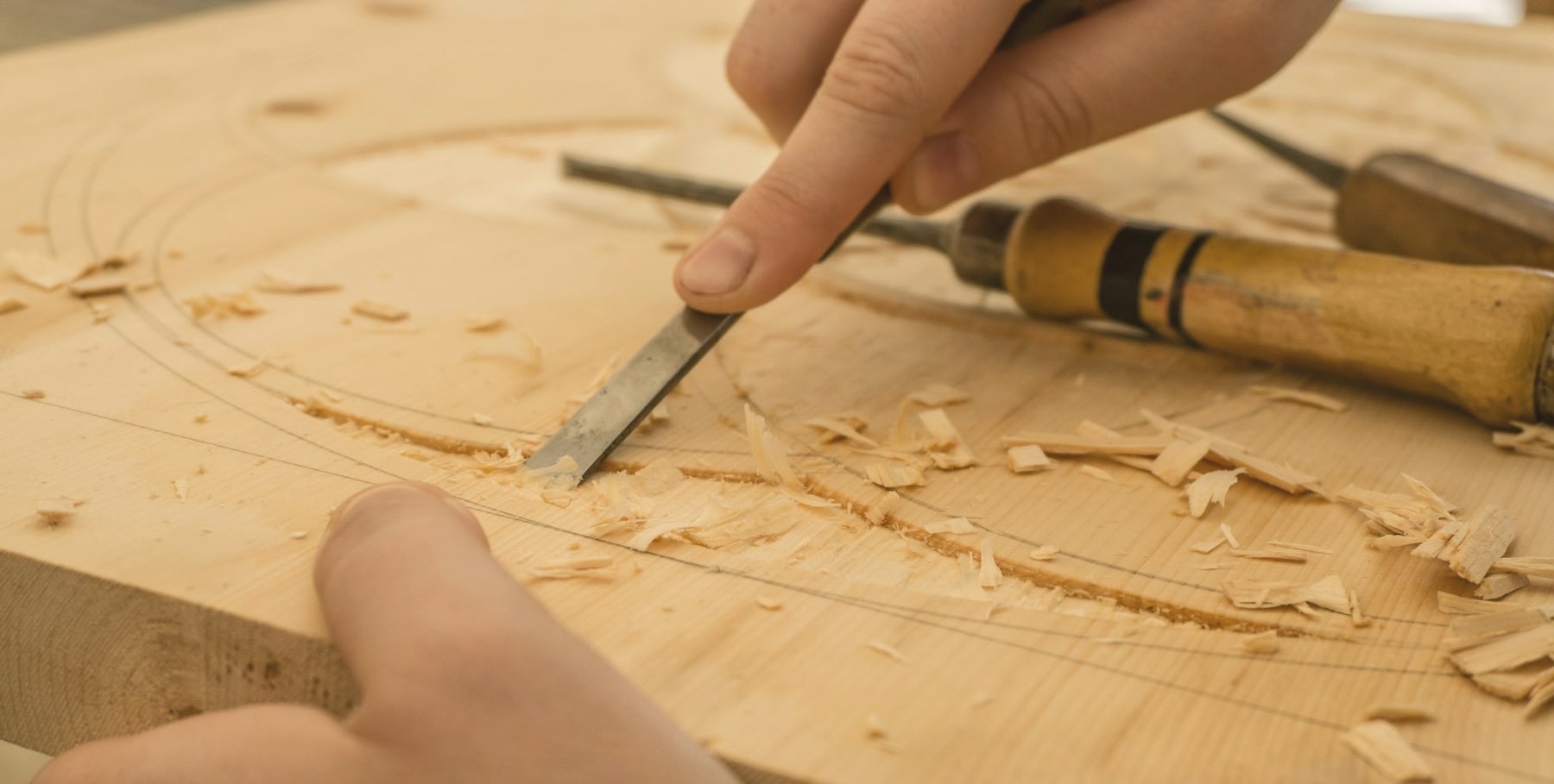 Mains d’artisan sculptant une planche de bois à la gouge