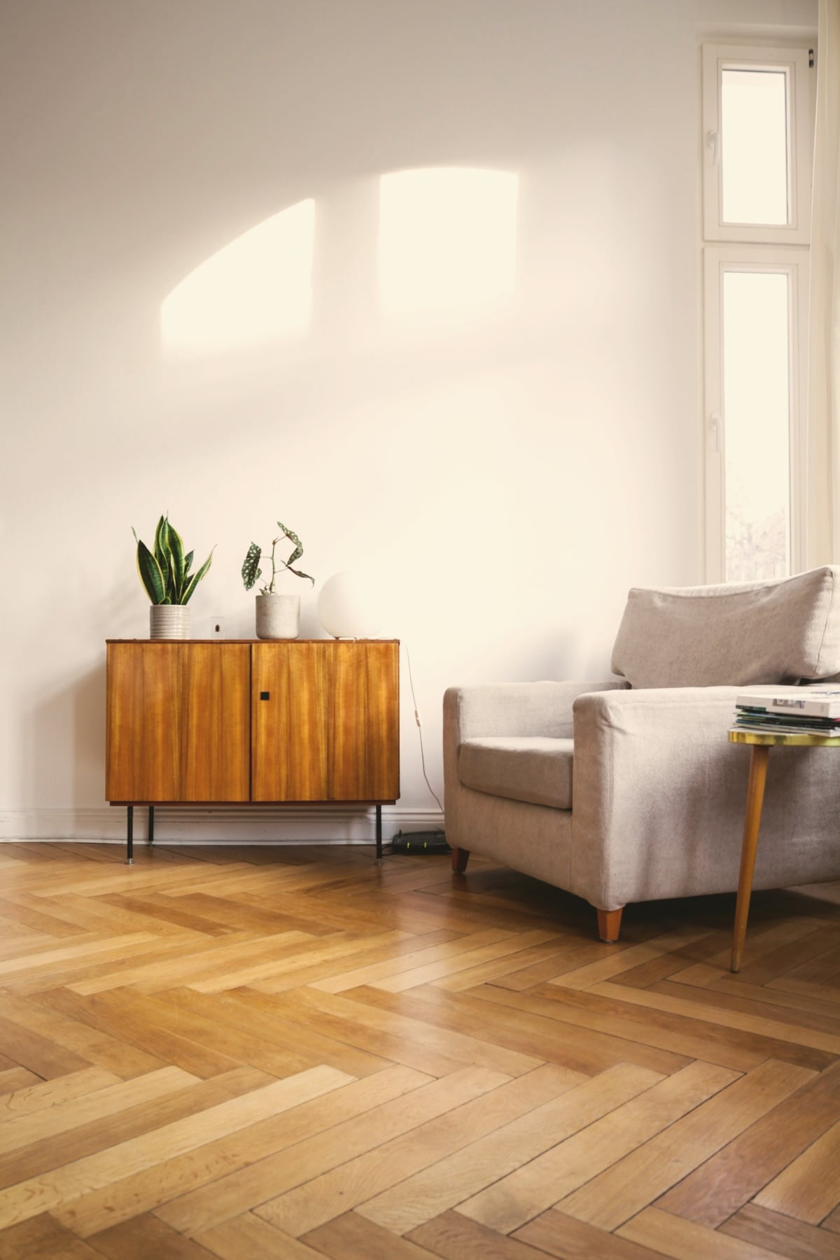Intérieur éditorial : buffet vintage en bois, fauteuil clair et parquet en chevrons
