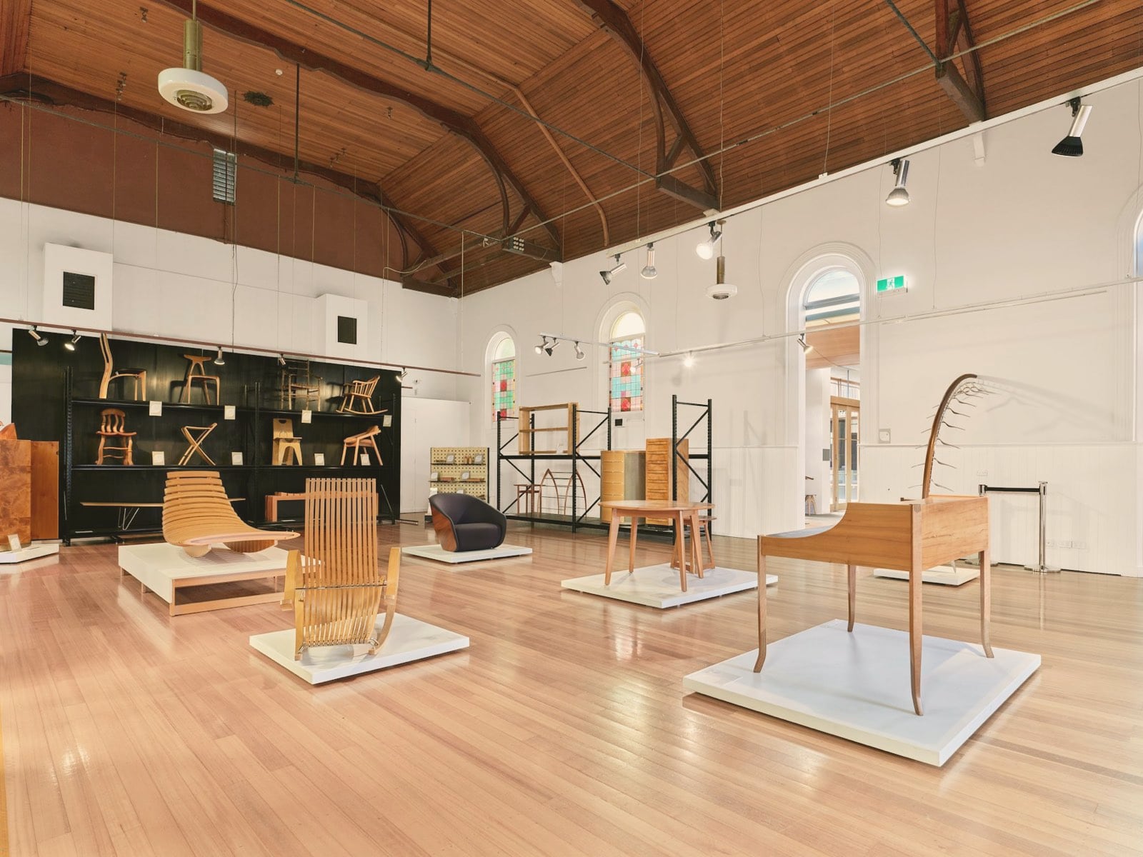 Mobilier en bois présenté sur des socles blancs dans une grande halle à charpente