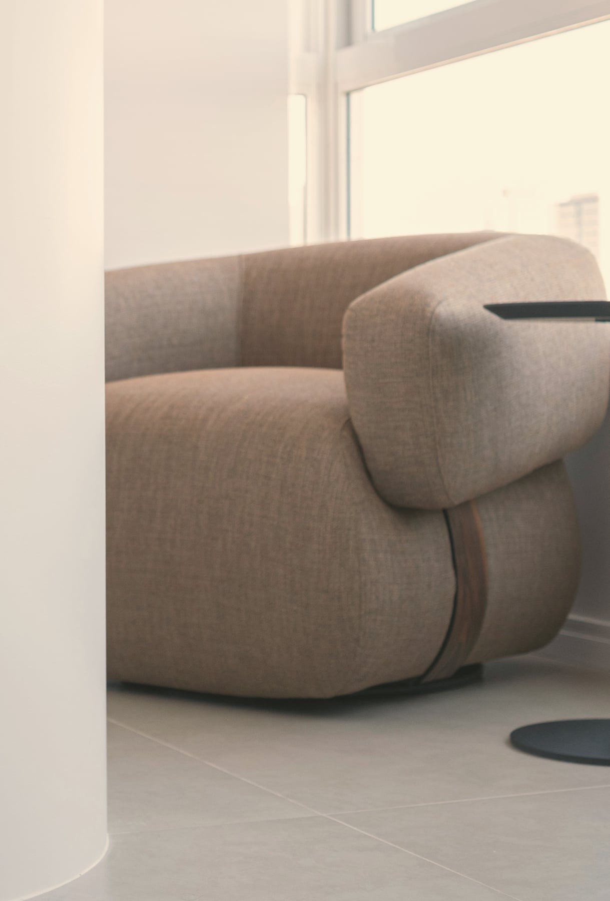 Fauteuil lounge aux formes courbes en tissu taupe près d’une grande jarre en terre blanche