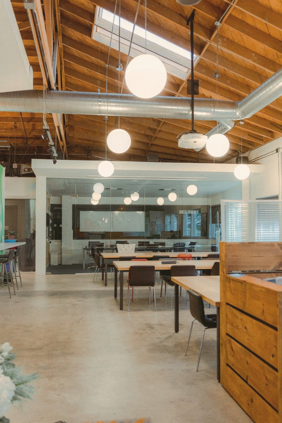 Espace de coworking sous charpente bois, globes lumineux et longues tables