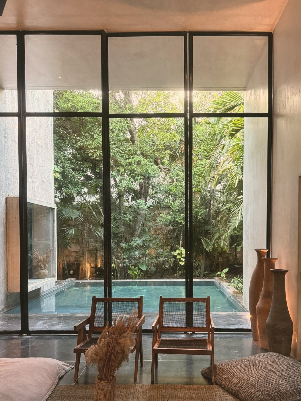 Pièce de vie aux matières brutes ouverte sur un patio et une piscine, coussins de sol et objets en terre