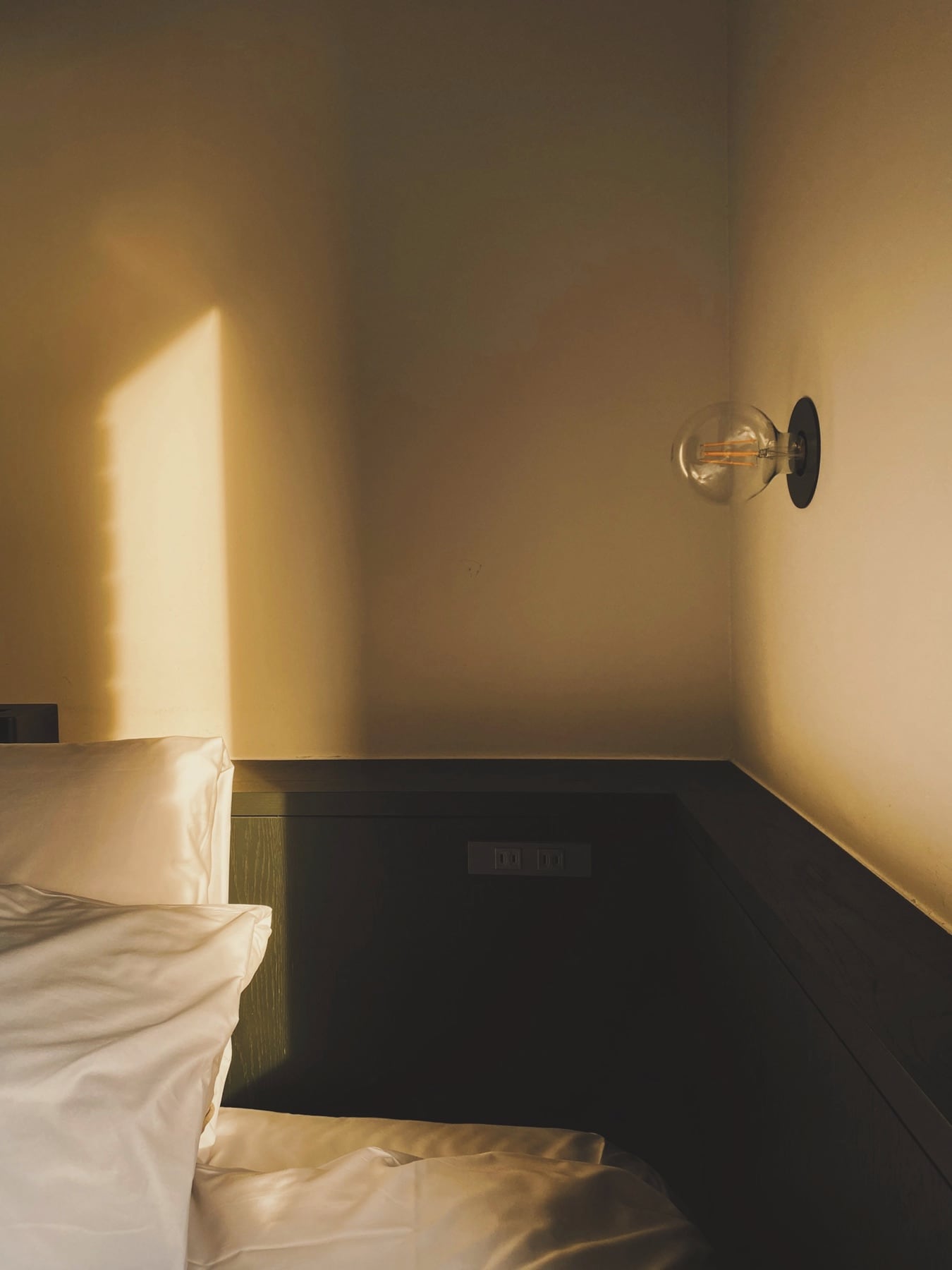 Tête de lit sombre et applique murale à globe dans une chambre baignée de lumière chaude