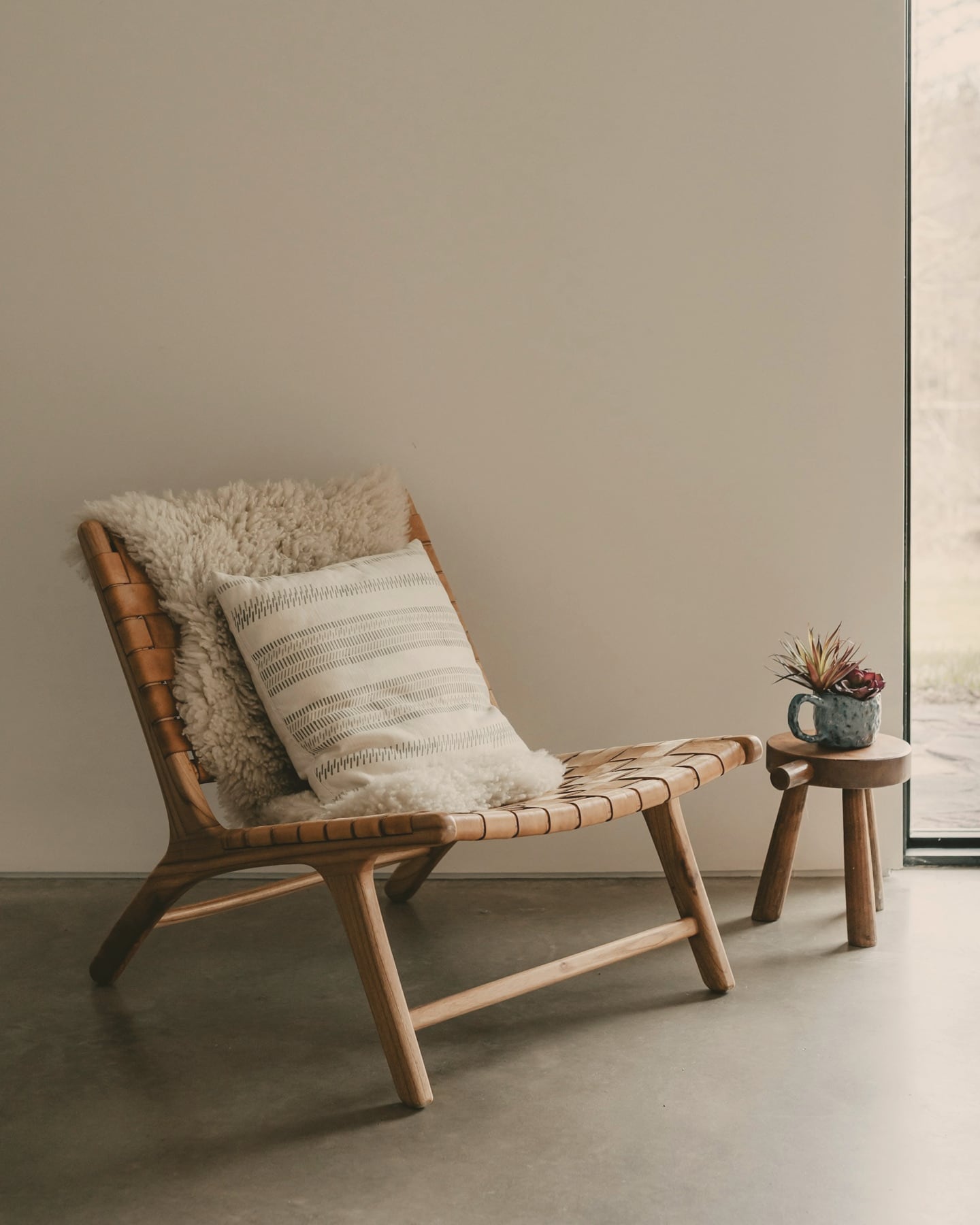 Coin lounge minimaliste : chaise longue en bois et cuir tressé, peau de mouton et petite table d’appoint