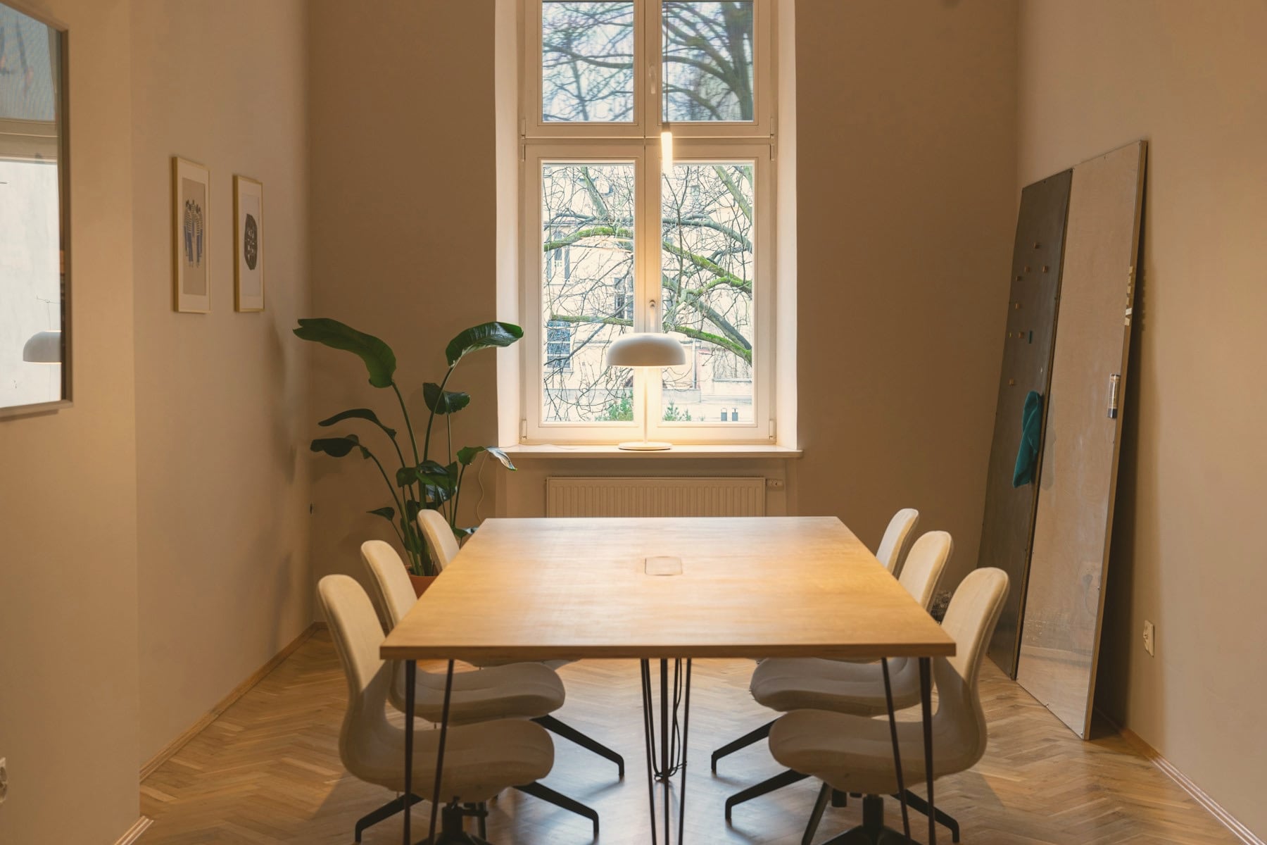 Salle de réunion sobre : table en bois, chaises crème, parquet en chevrons et grande fenêtre